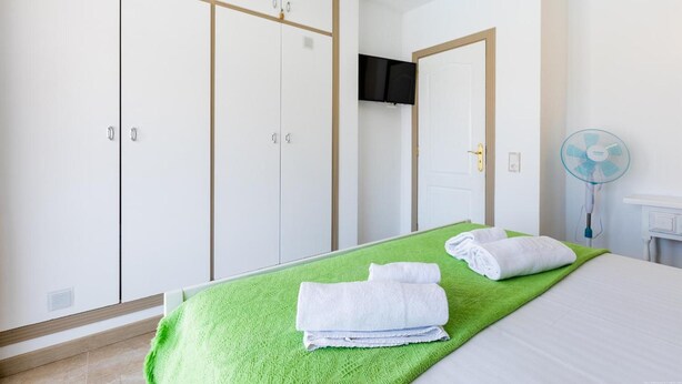 A hotel room with a bed, green blanket, white towels, a TV, and a fan. - Las Floritas (Arona)