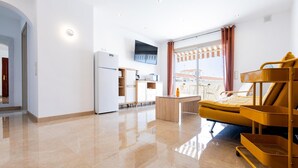 A modern hotel room with a kitchen area, a sofa, a TV, and a large window with curtains. - Las Floritas (Arona)
