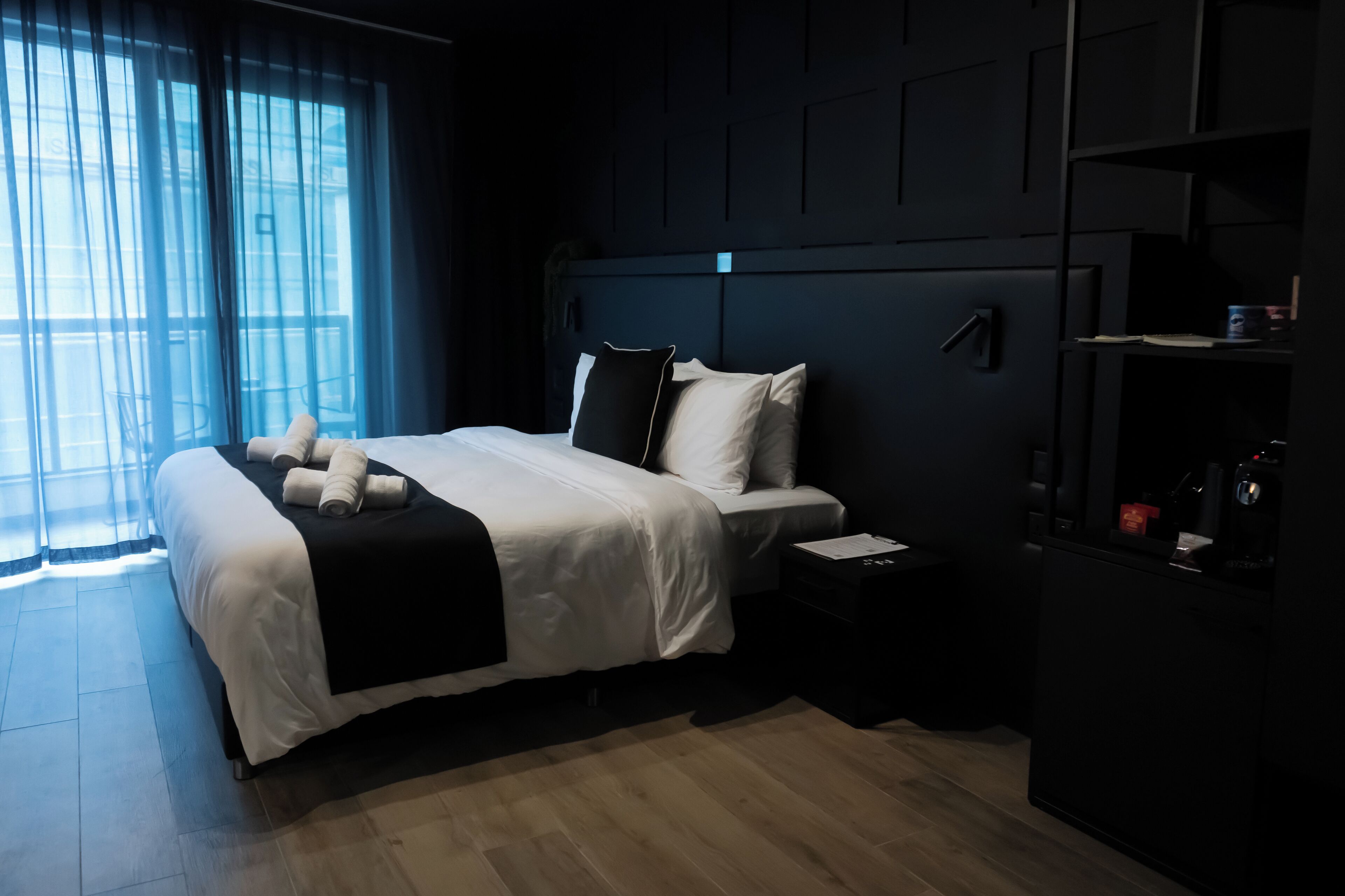 A modern hotel room with a large bed, a bedside table, and a built-in wardrobe.
