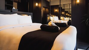 A modern hotel room with a large bed, a bedside table, a mirror, and wall-mounted lights.