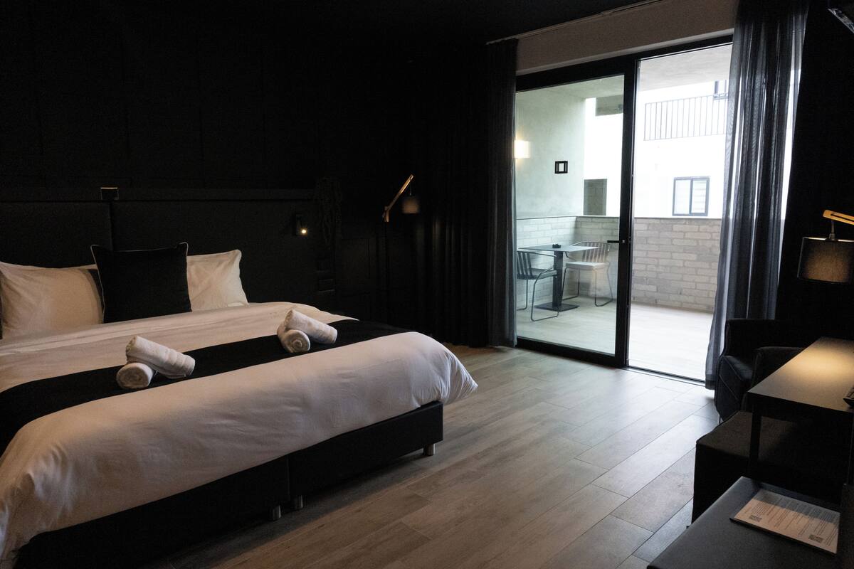 A modern hotel room with a large bed, a small desk, and a sliding glass door leading to a balcony.