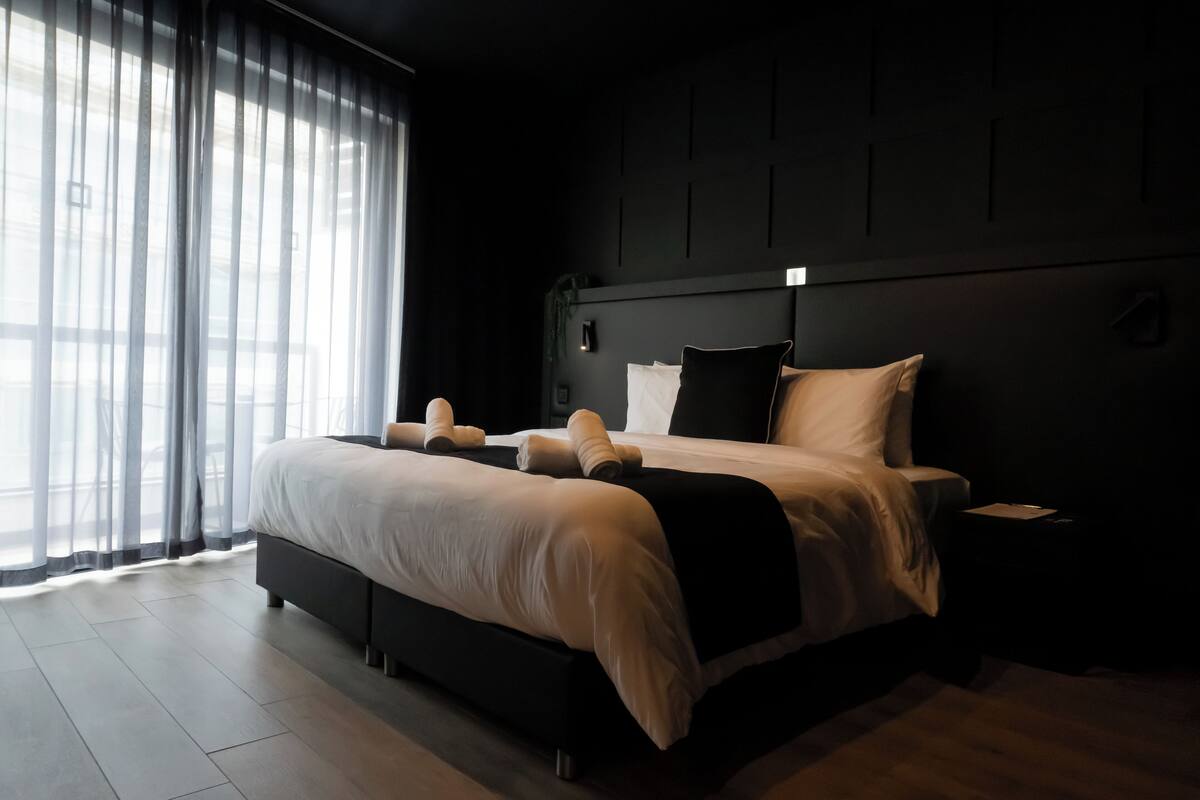 A modern bedroom with a large bed, a bedside table, and a window with sheer curtains.