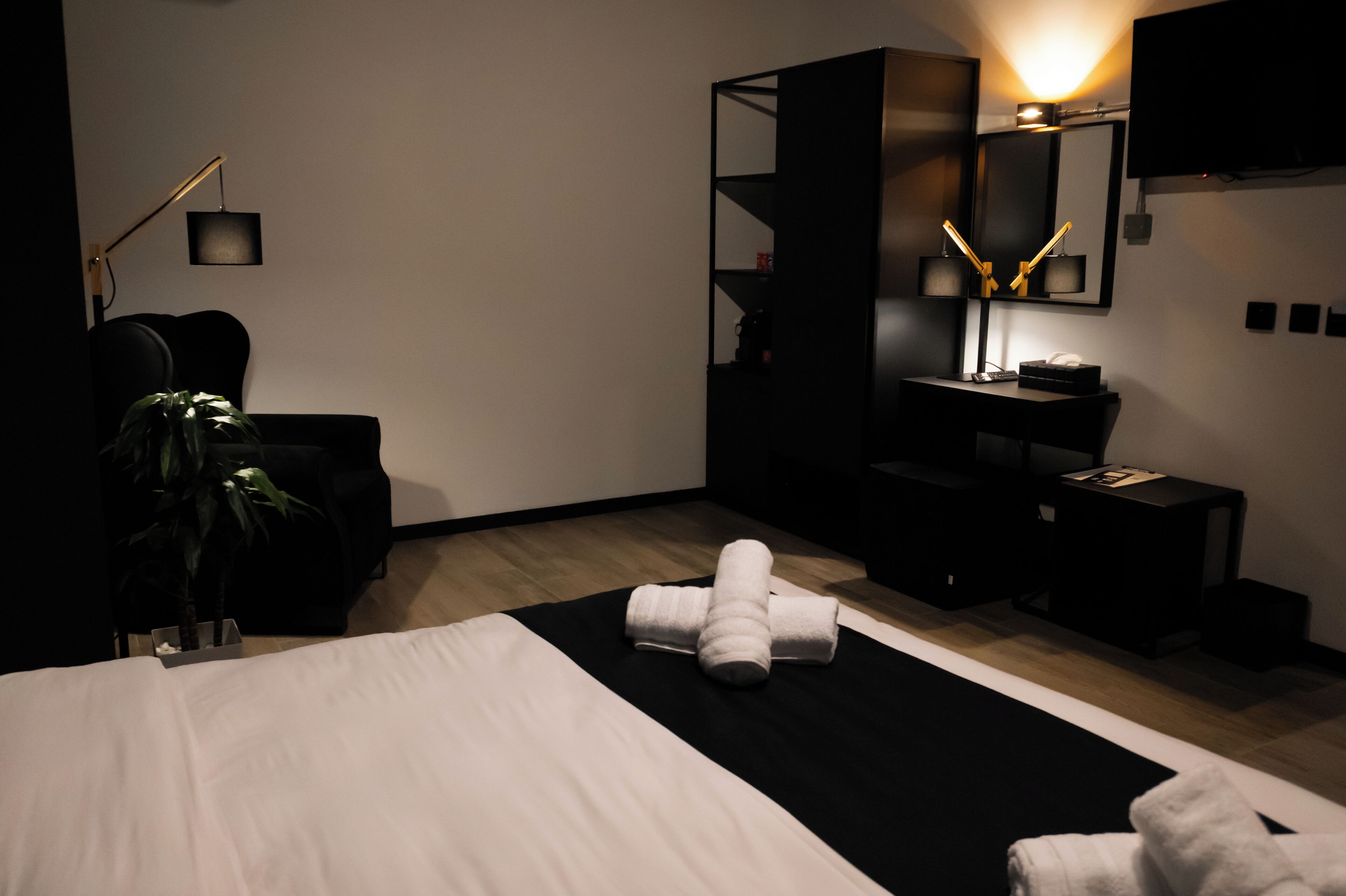 A modern hotel room with a large bed, a black desk, a mirror, and a TV.