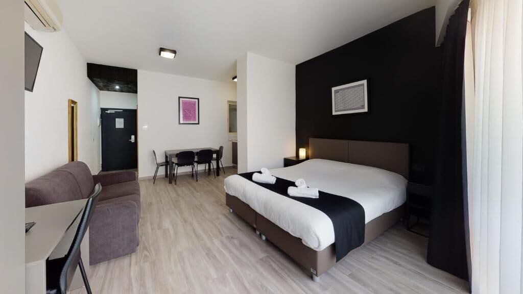 A modern hotel room with a large bed, a desk, and a sofa.