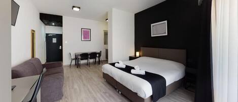 A modern hotel room with a large bed, a desk, and a sofa.