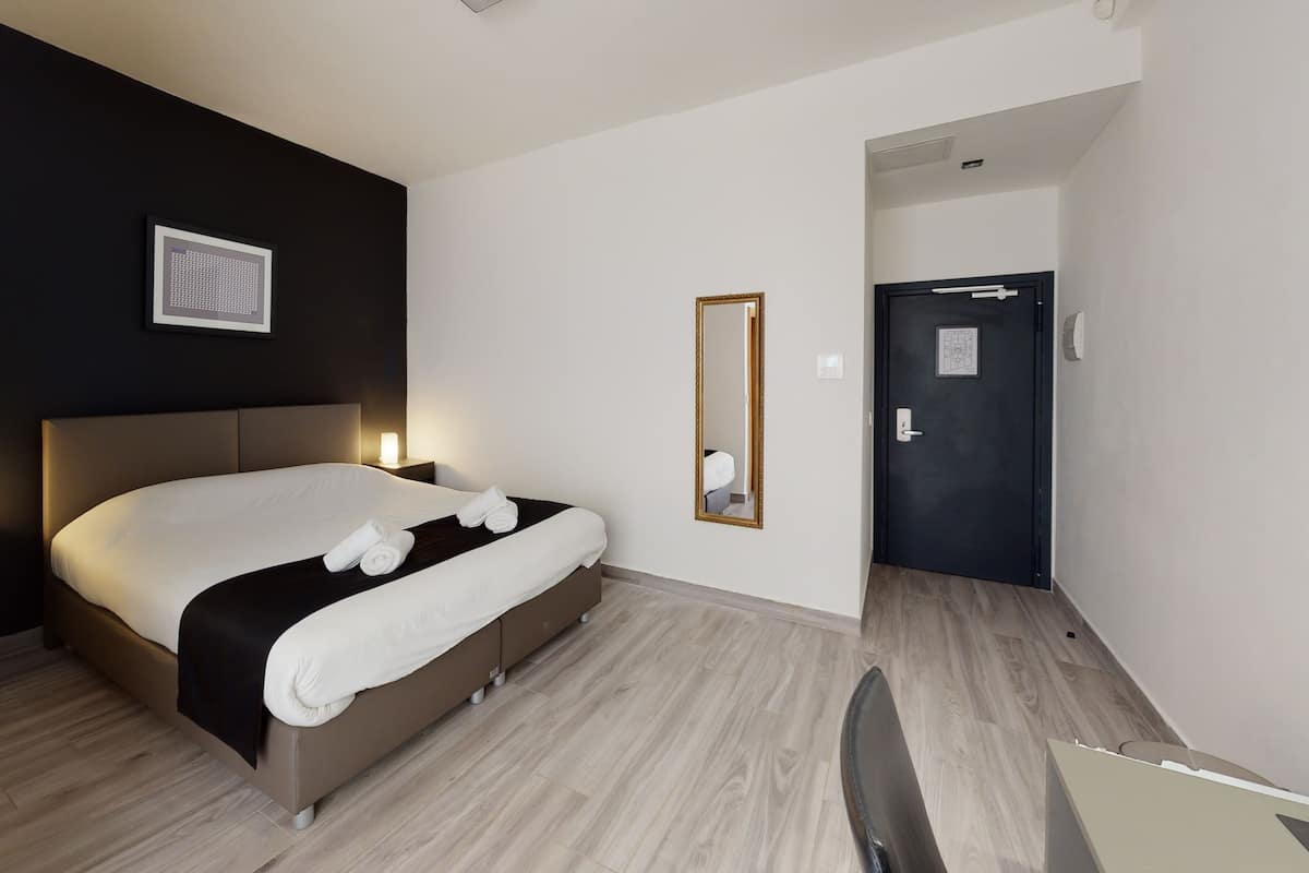 A modern hotel room with a large bed, bedside lamps, a framed picture on the wall, a mirror, and a door.