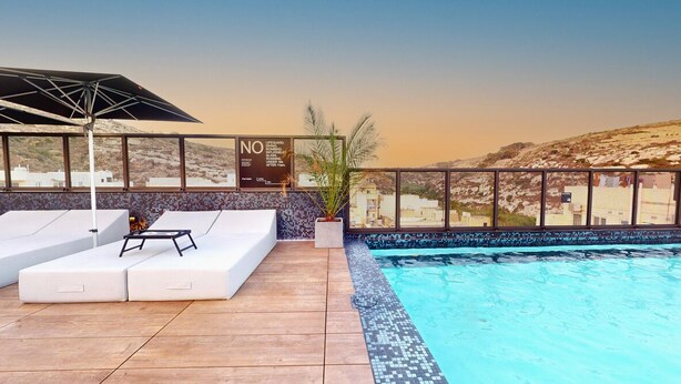 A rooftop pool area with white lounge chairs, a small table, and a sign with text.