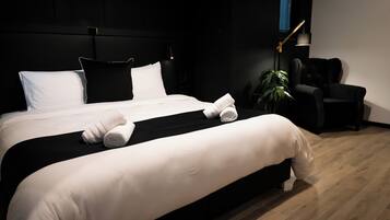 Een moderne hotelkamer met een groot bed, zwart-wit beddengoed, een zwarte fauteuil, een bureaulamp en een kamerplant.