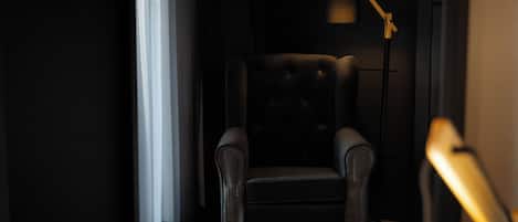 A dark room with a single leather armchair and a floor lamp.