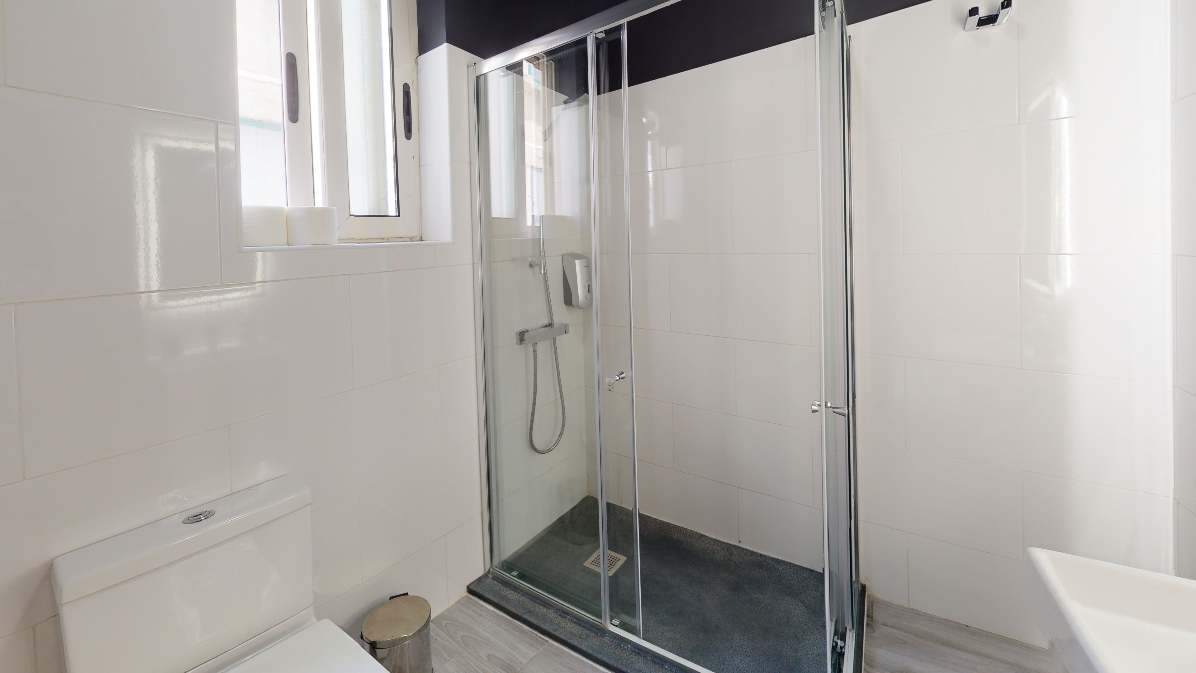 A modern bathroom with a glass-enclosed shower, white tiles, a toilet, and a sink.