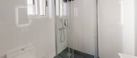 A modern bathroom with a glass-enclosed shower, white tiles, a toilet, and a sink.