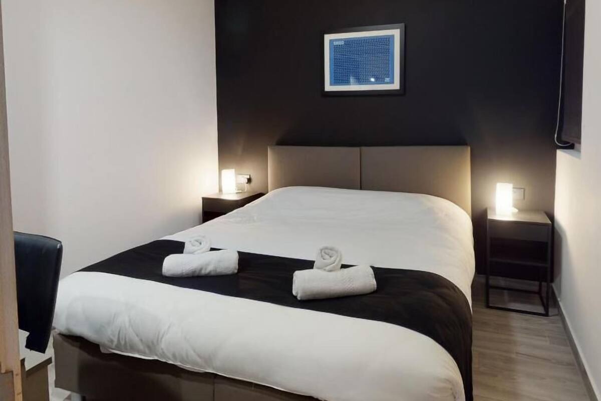 A hotel room with a large bed, two bedside tables with lamps, a flat-screen TV mounted on the wall, and a framed picture above the bed.