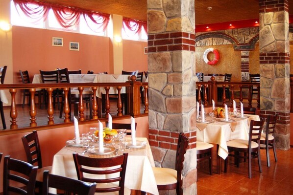 A restaurant with multiple tables, wooden chairs, and a stone fireplace. - Amaris (Sunny Beach)