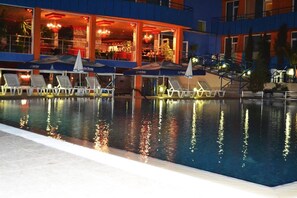 A swimming pool with lounge chairs and umbrellas, a building with a bar area, and a staircase leading to an upper level.