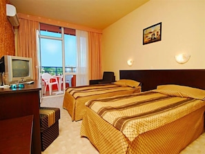 A hotel room with two beds, a television, a desk, and a balcony with chairs. - Amaris (Sunny Beach)