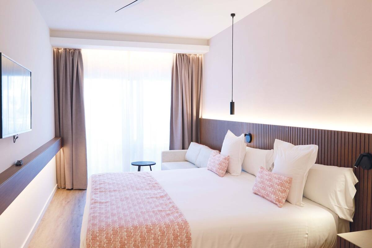 Une chambre d’hôtel moderne avec un grand lit, un téléviseur fixé au mur et une petite table.