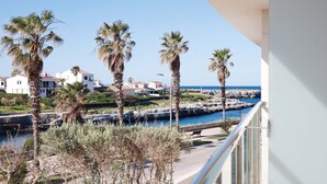 A balcony overlooking a coastal area with palm trees, a rocky shoreline, and residential buildings. - Hotel Seth Port Ciutadella (Ciutadella de Menorca)