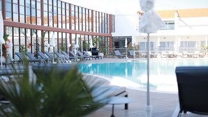 A swimming pool with lounge chairs and umbrellas, surrounded by a modern building with large windows.