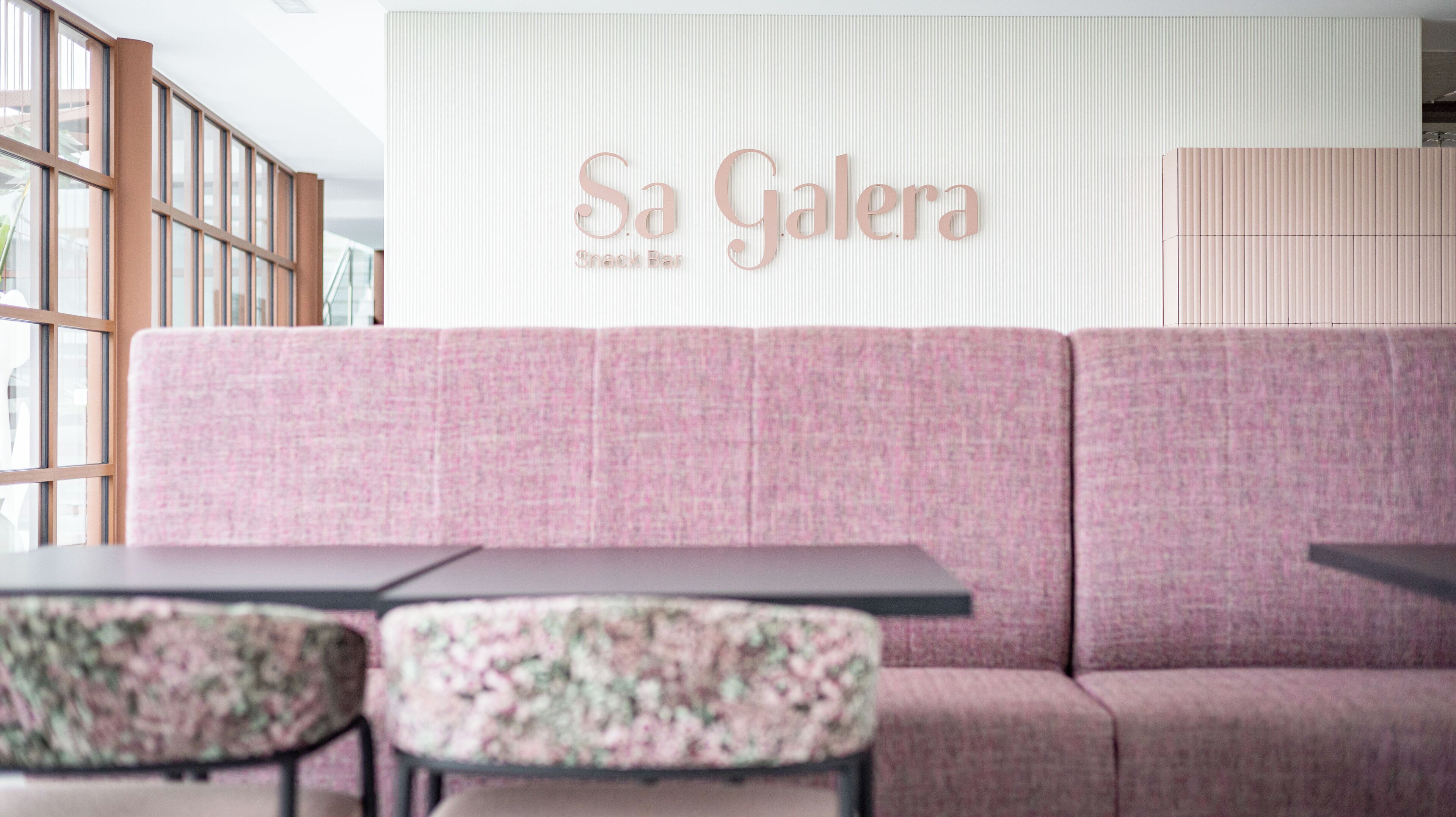Un sofá rosa y dos sillones a juego en un interior moderno, con un cartel que dice 'Sa Galera' en la pared.