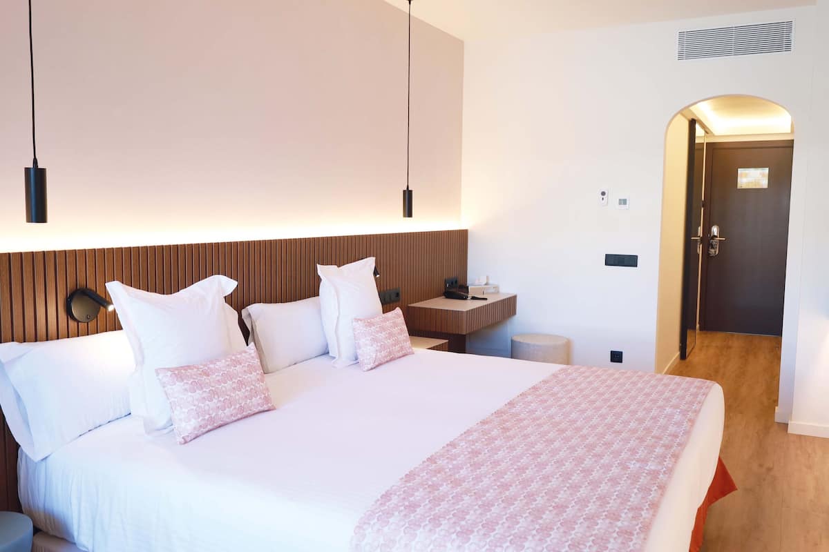 Ein modernes Hotelzimmer mit einem großen Bett, Nachttischen, einem Fernseher und einem hölzernen Kopfteil.
