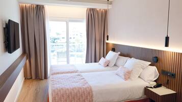 A hotel room with a bed, a TV, a bedside table, and a view of the outdoors.