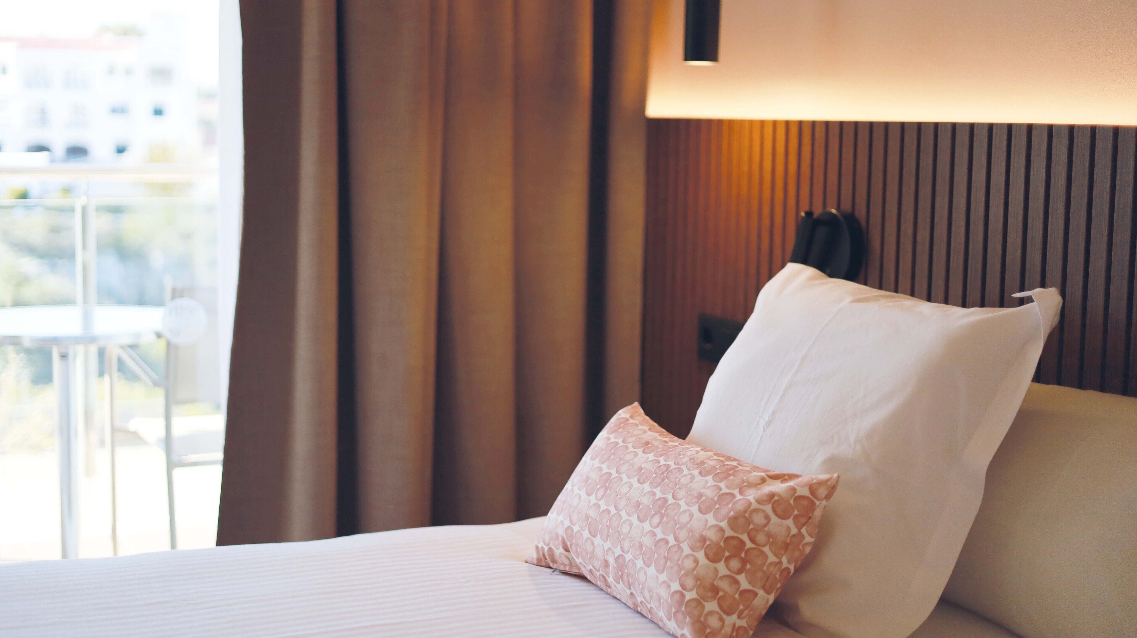 Habitación de hotel con una cama, una ventana con cortinas y vistas a edificios.