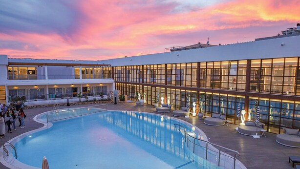 A swimming pool with a deck, lounge chairs, and a building with large windows.