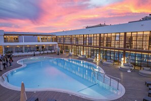 En swimmingpool med en terrass, solstolar och en byggnad med stora fönster.
