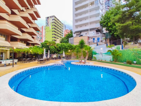 A swimming pool surrounded by outdoor seating and greenery, with buildings in the background. - Picasso - Fincas Benidorm (Benidorm)