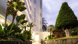 A modern building with Dorothea signage, a stone wall, and a well-maintained garden with various plants. - Apartamentos Dorotea (San Bartolomé de Tirajana)