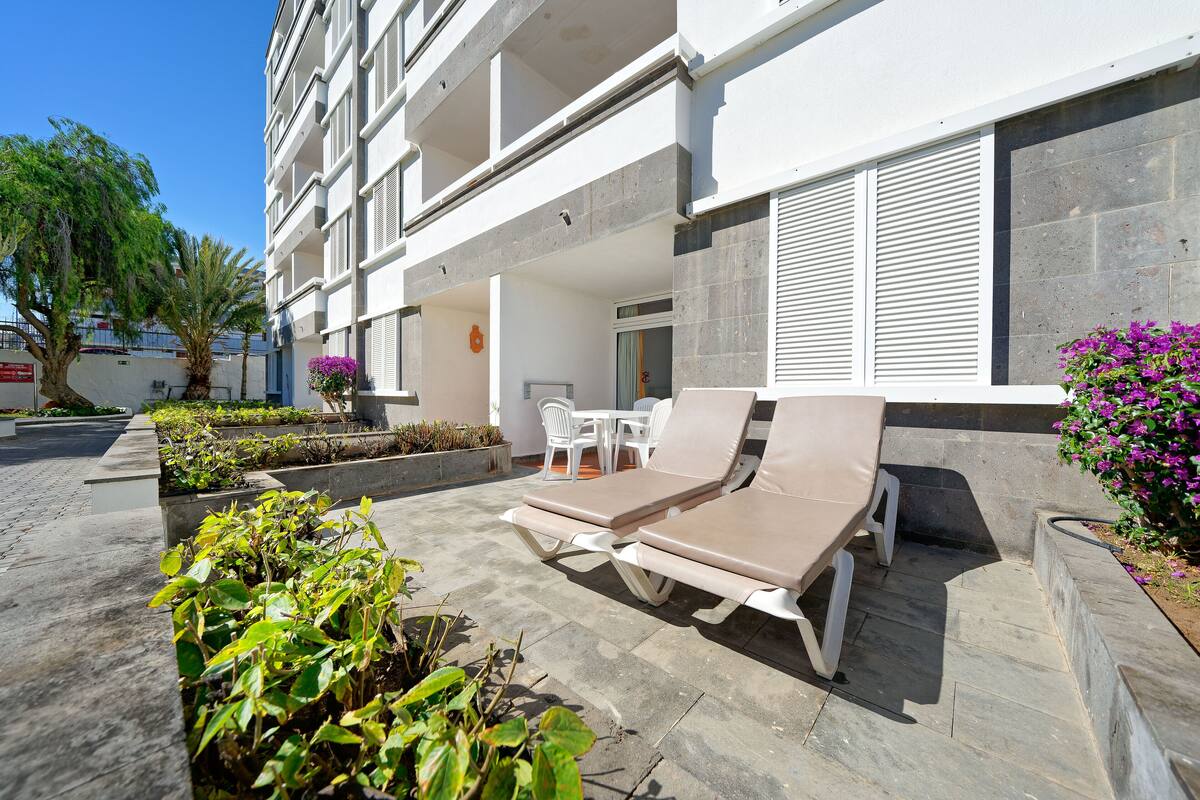 A modern building with a balcony, outdoor seating area, and potted plants.