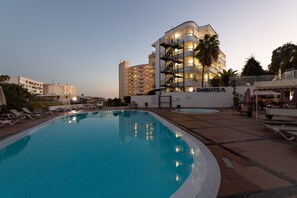 A swimming pool with lounge chairs, a Dorotea building, and a palm tree. - Apartamentos Dorotea (San Bartolomé de Tirajana)