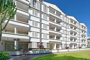 A multi-story hotel with balconies, a paved entrance area, and a well-maintained garden.