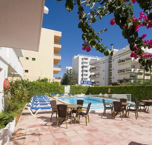 A poolside area with lounge chairs and tables, a swimming pool, and surrounding greenery. - Green Line Bon Sol Apartamentos (Ibiza Town)