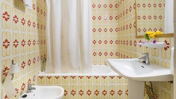 A bathroom with patterned wallpaper, a bathtub, a sink, and a bidet.