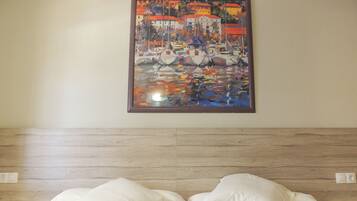 Une chambre d’hôtel avec un lit, deux oreillers, une tête de lit en bois et un tableau coloré accroché au mur.