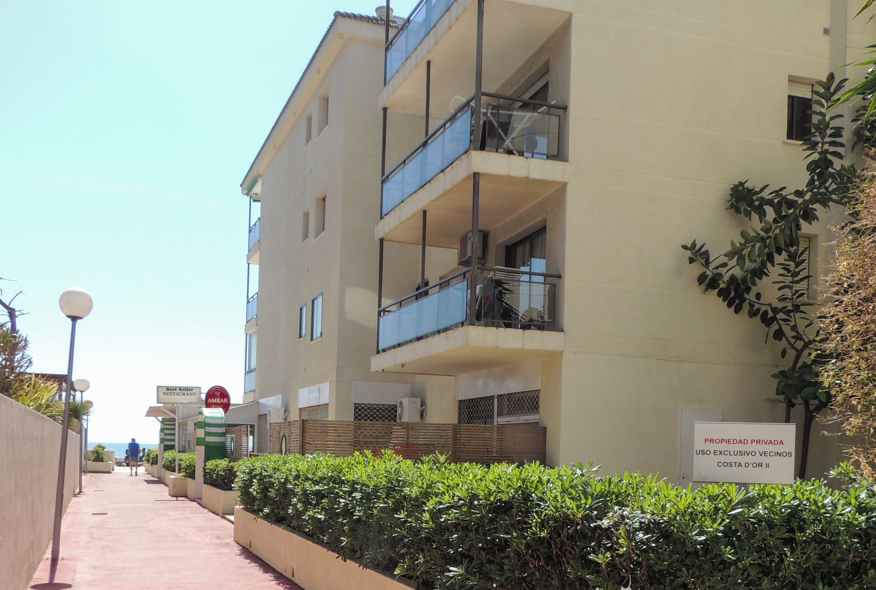 Un edifici d'alguns pisos amb balcons, un senyal de propietat privada i un camí vorejat de vegetació.