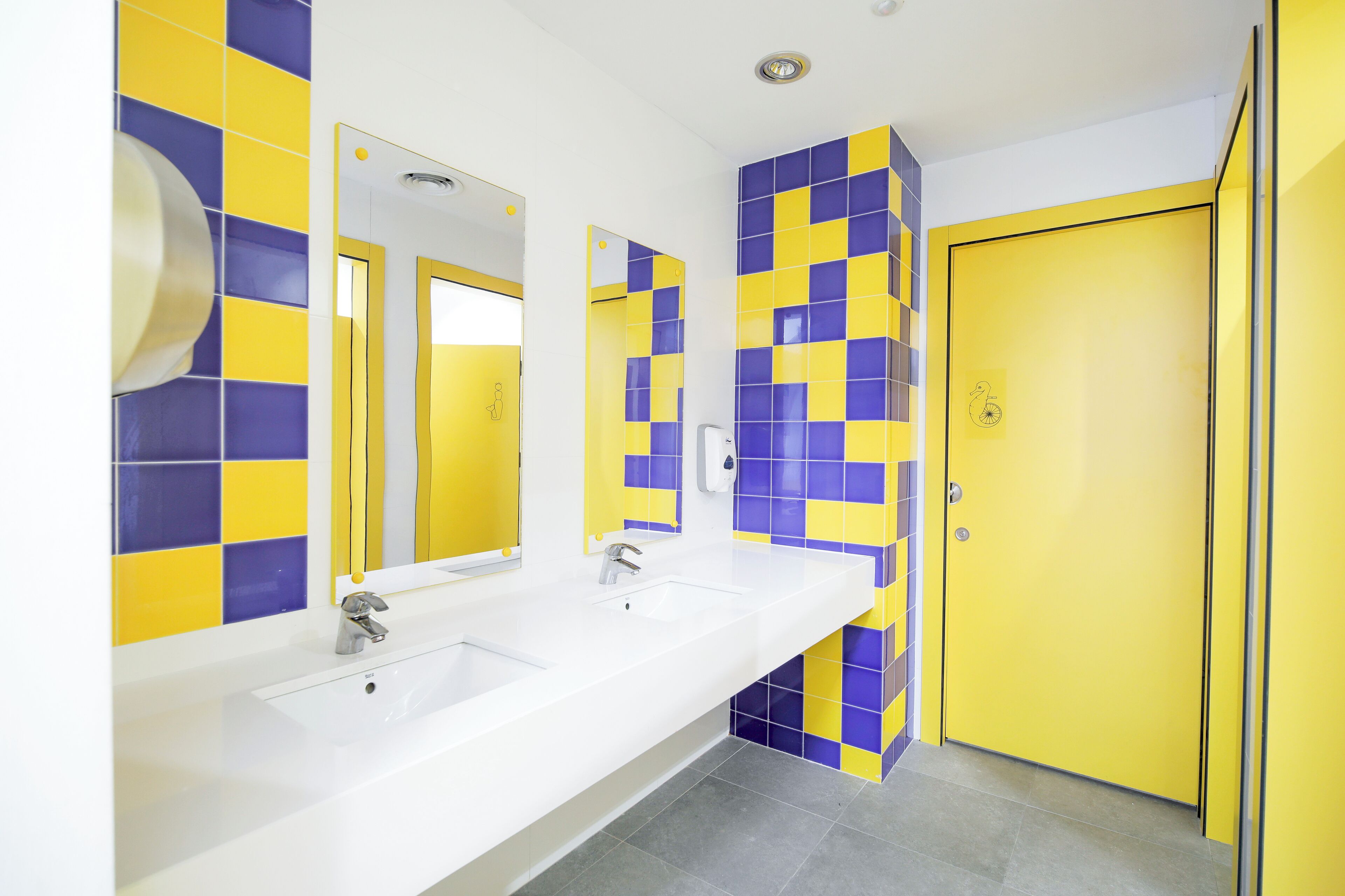 Un baño con dos lavabos, un espejo y una puerta amarilla.