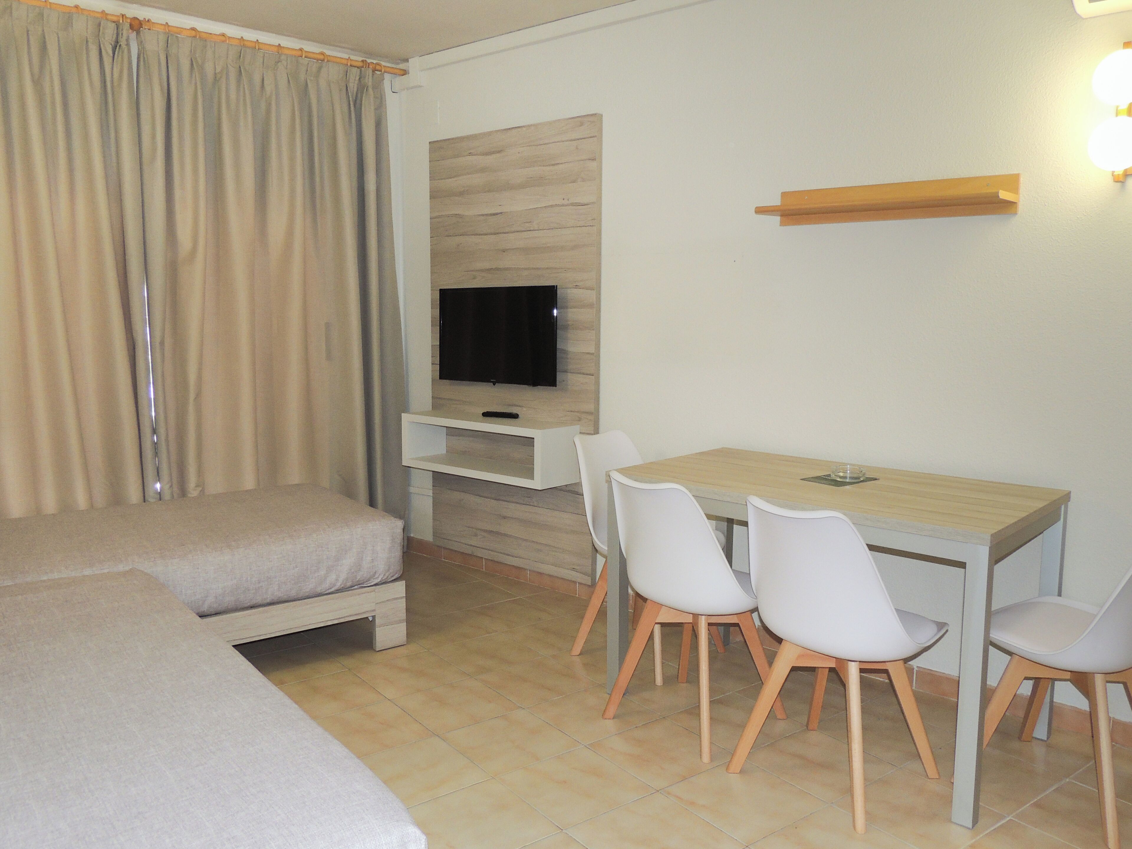Habitació d'hotel amb un llit, una taula amb cadires, un televisor i un panell de paret de fusta.