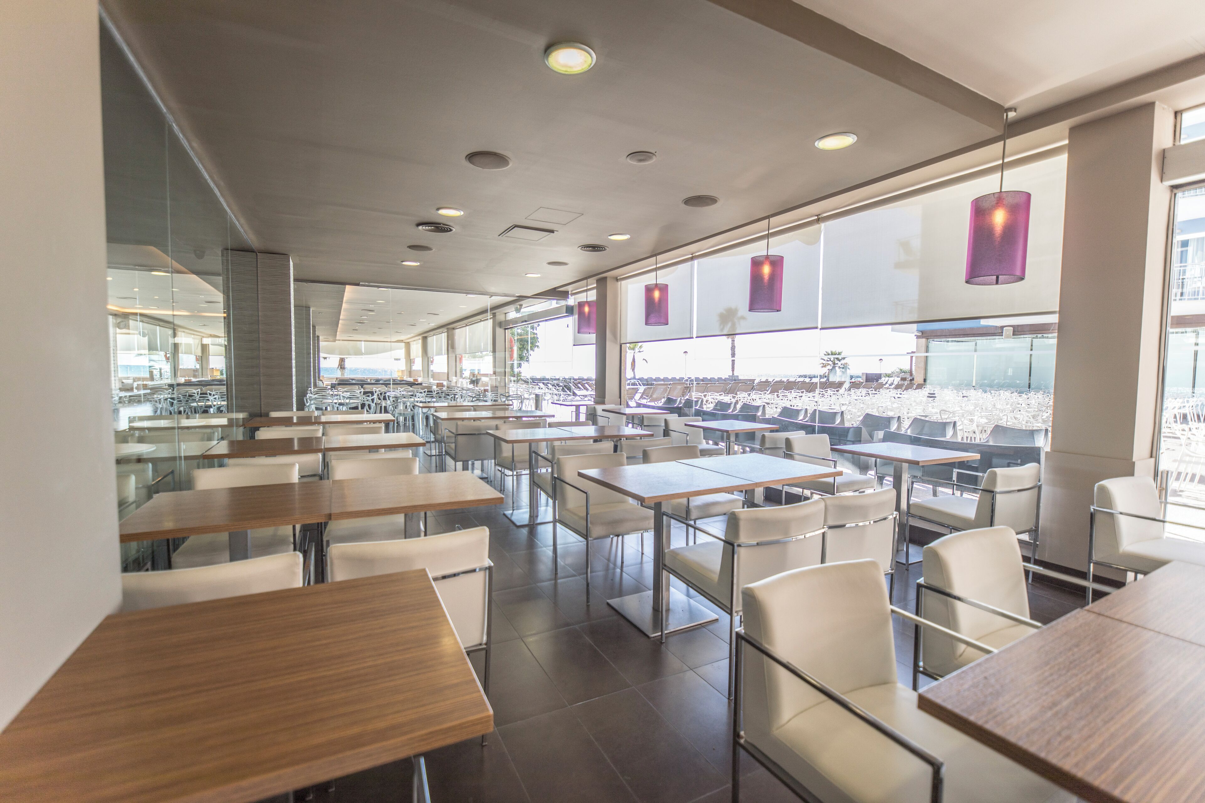 A modern dining area with tables and chairs, large windows, and pendant lights.