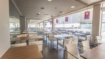 A modern dining area with tables and chairs, large windows, and pendant lights.