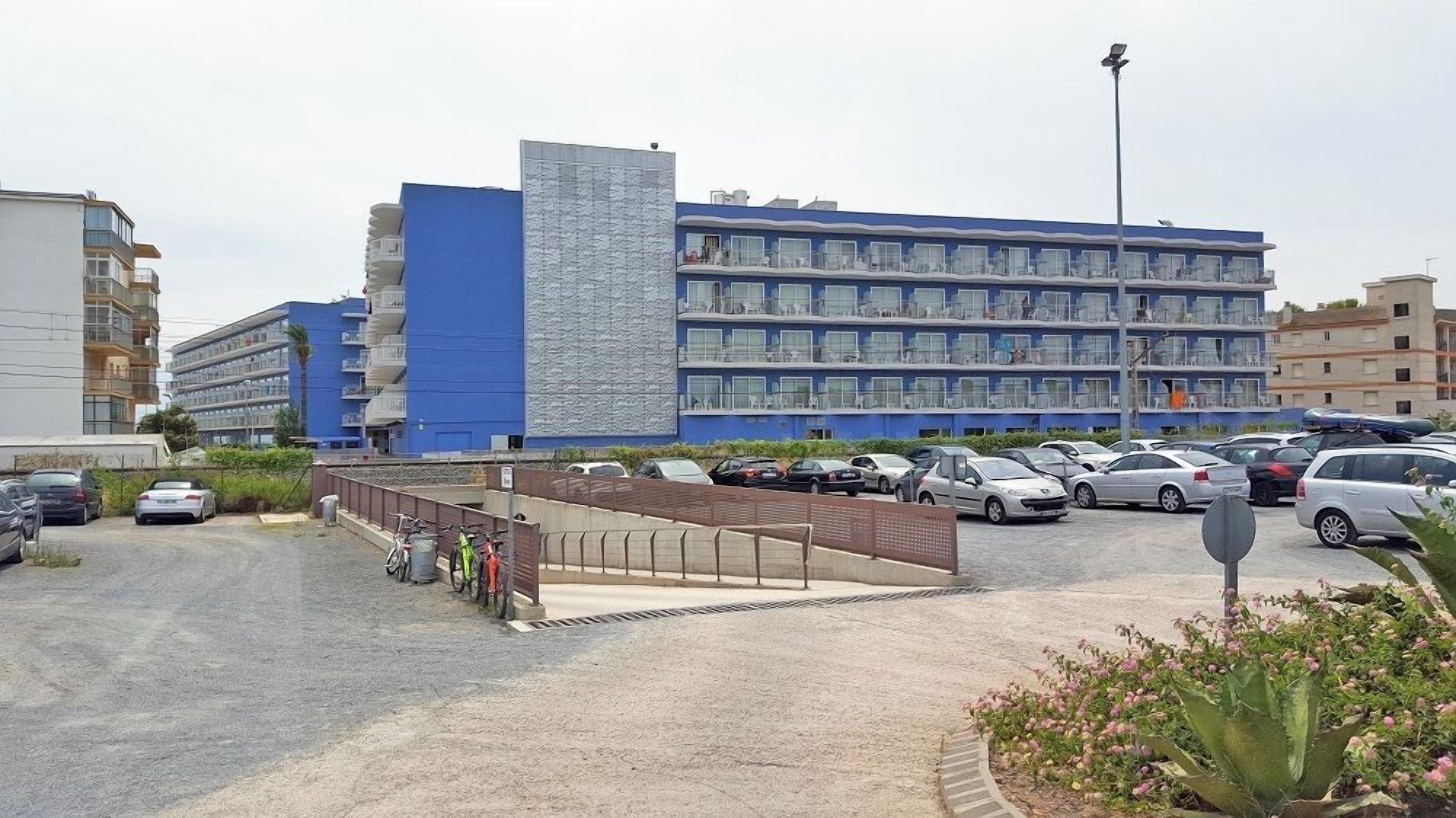 A parking lot with several cars and a building with multiple balconies in the background.