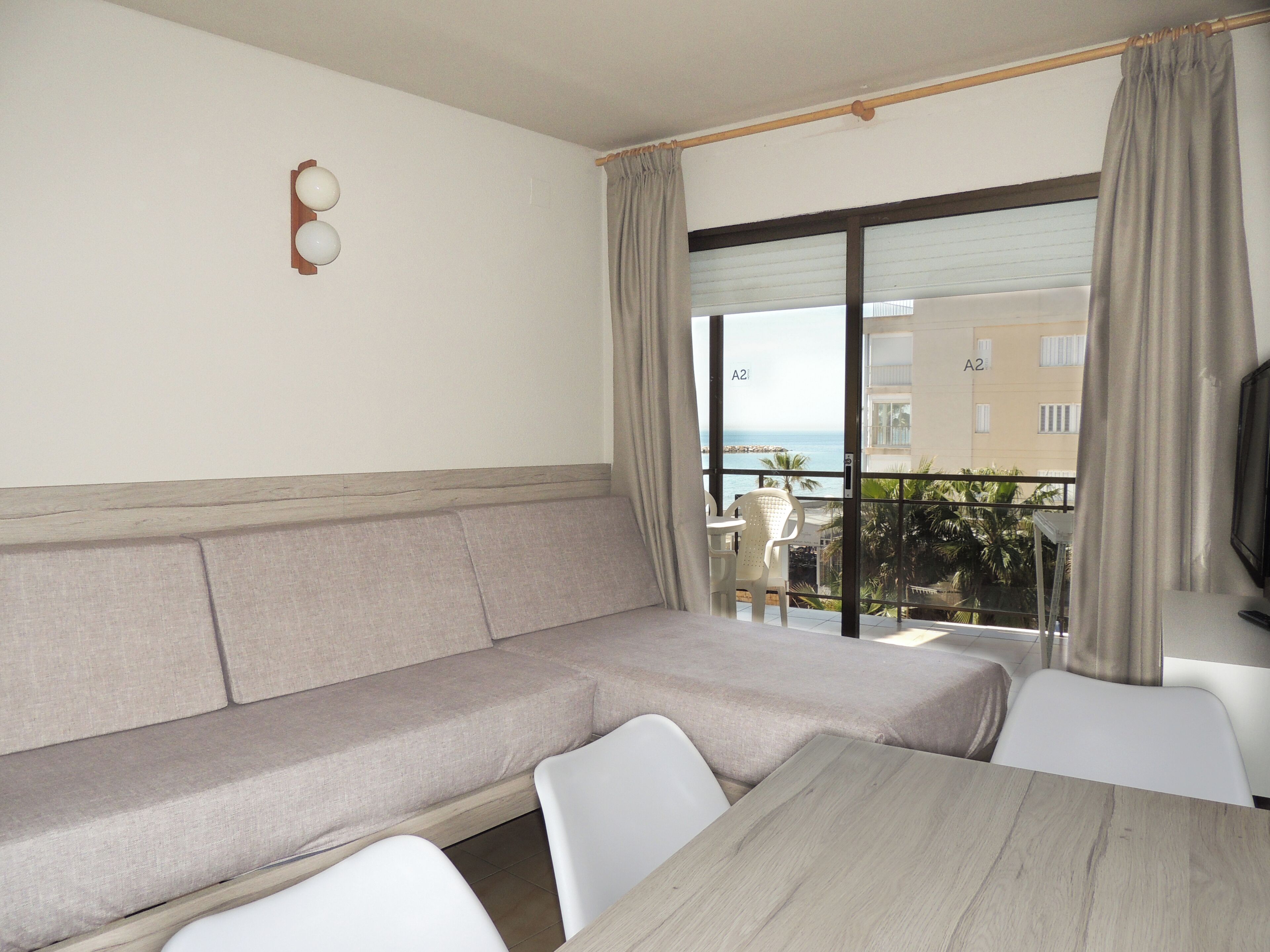A modern living room with a beige sofa, a wooden table, and a view of the sea through large windows.