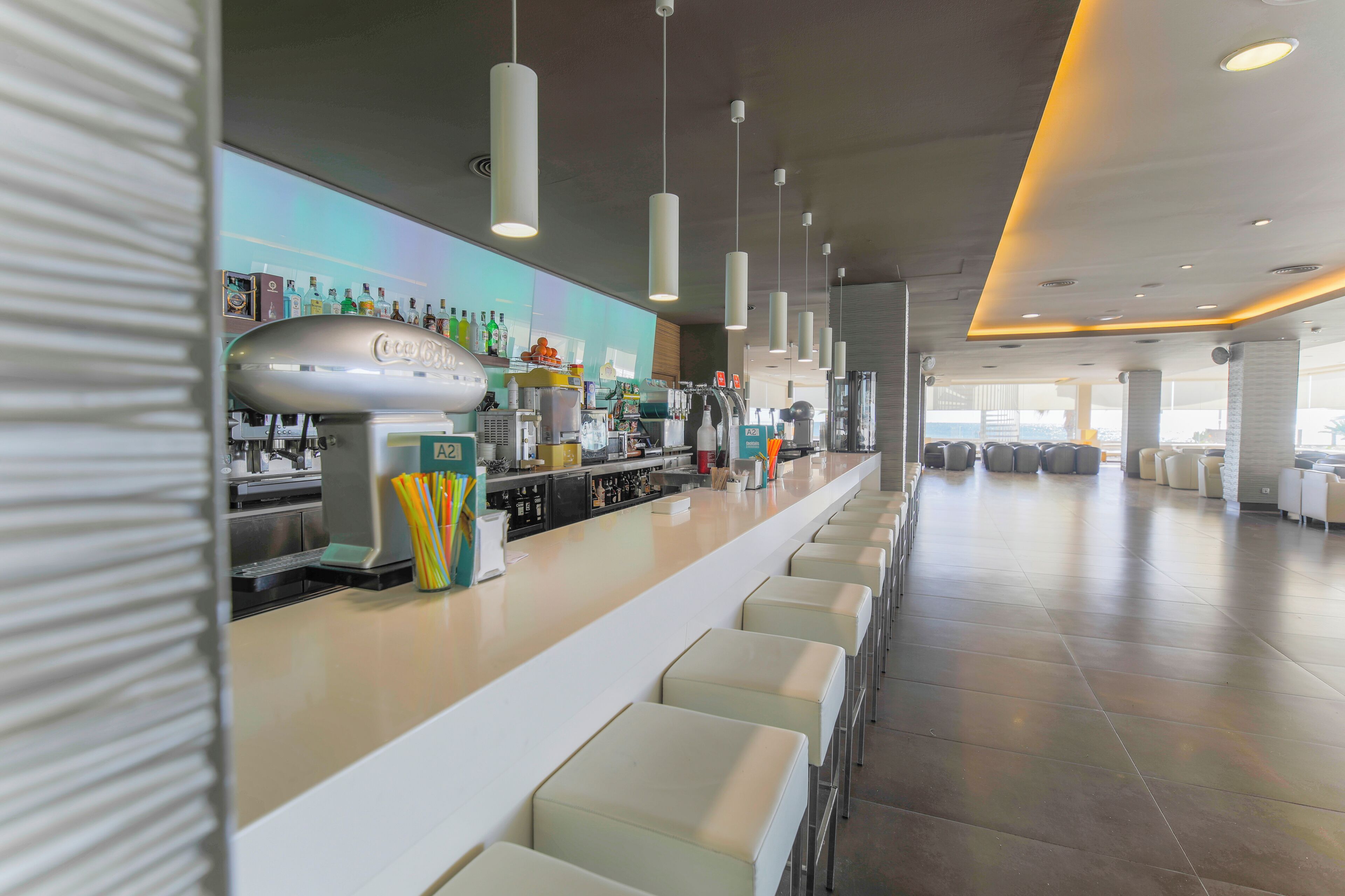 Zona de bar moderna amb una barra llarga, diverses opcions de seients i una varietat d'equipatge de bar.