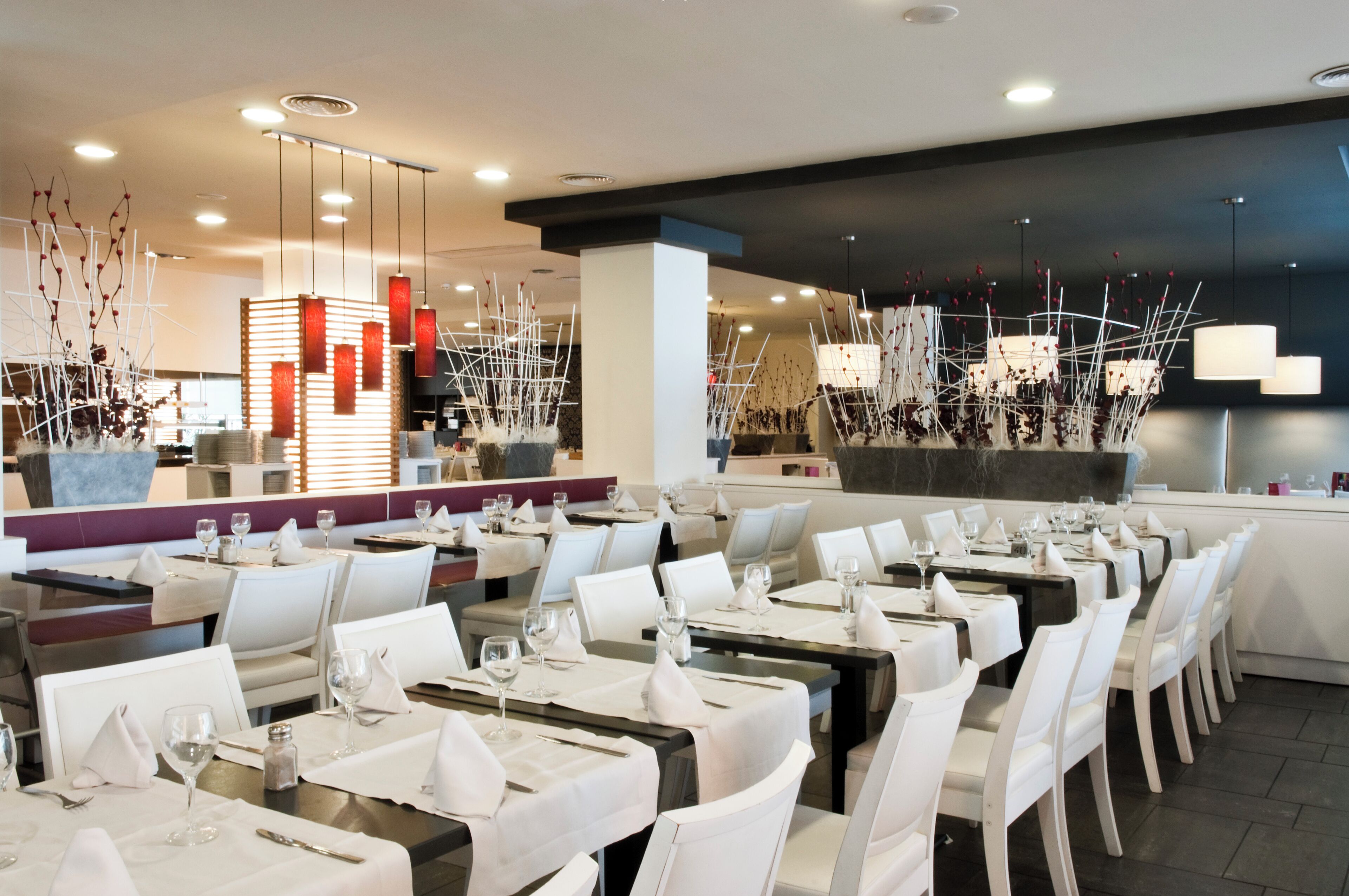 En modern restaurang med vita bord och stolar, snyggt arrangerade sittplatser och stilren belysning.