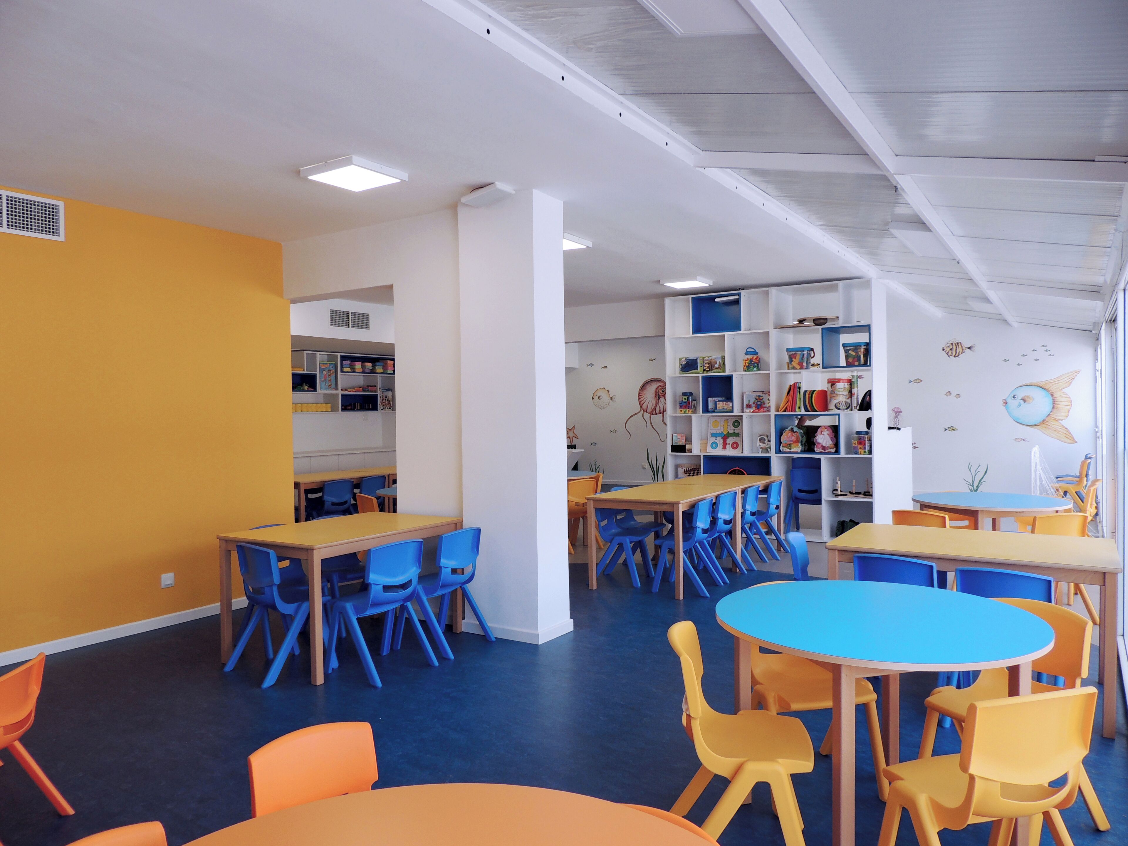 Un cuarto de juegos para niños con mesas y sillas, una estantería y un mural en la pared.