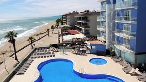 A hotel with a pool, beach view, and multiple balconies.