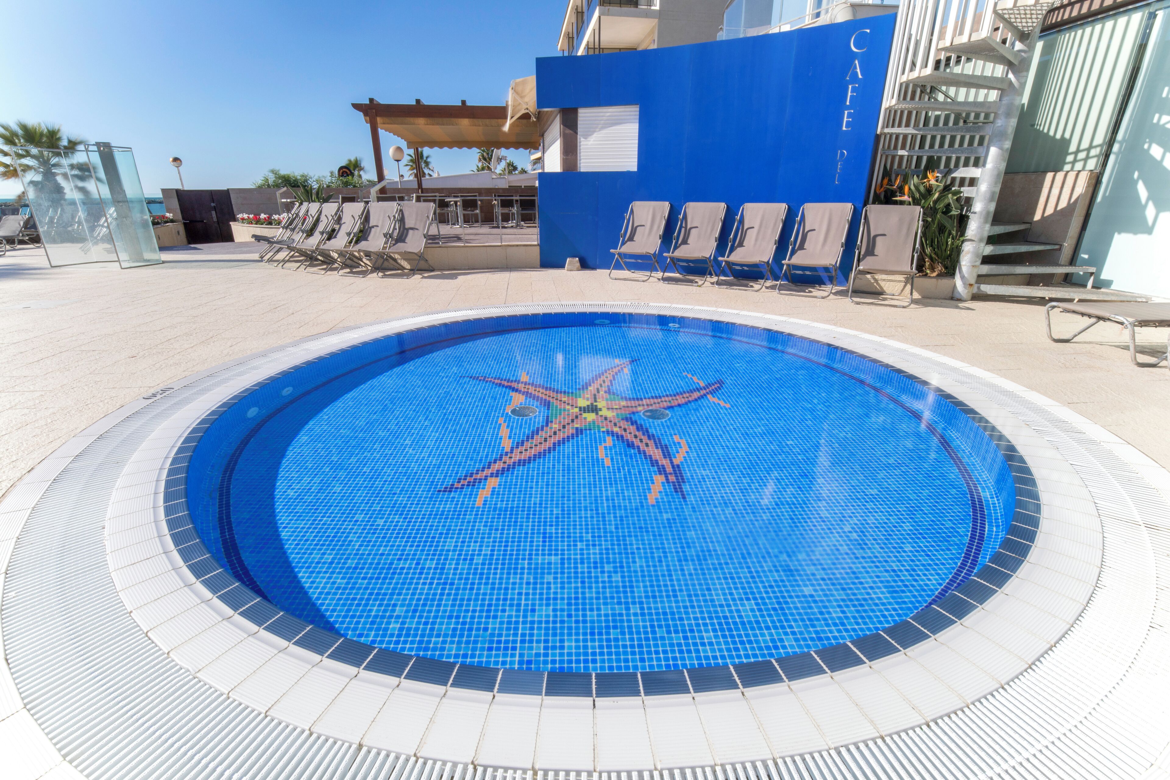 A circular pool with a starfish decoration, surrounded by lounge chairs and a blue wall with the word "CAFE".