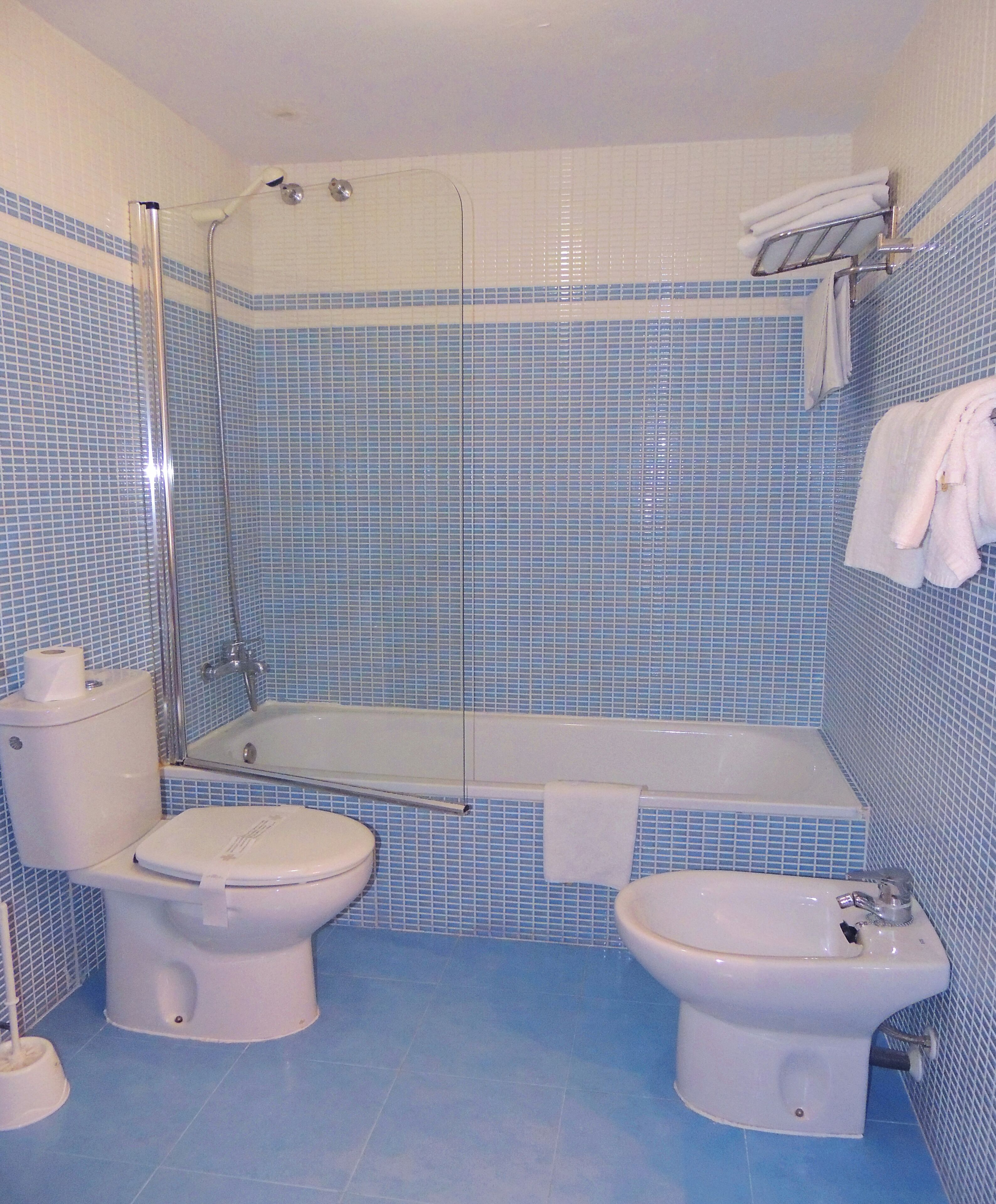 A bathroom with a toilet, bidet, and bathtub, all with blue-tiled walls.