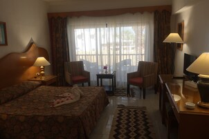 A hotel room with a bed, two armchairs, a small table, a TV, and a window with curtains.